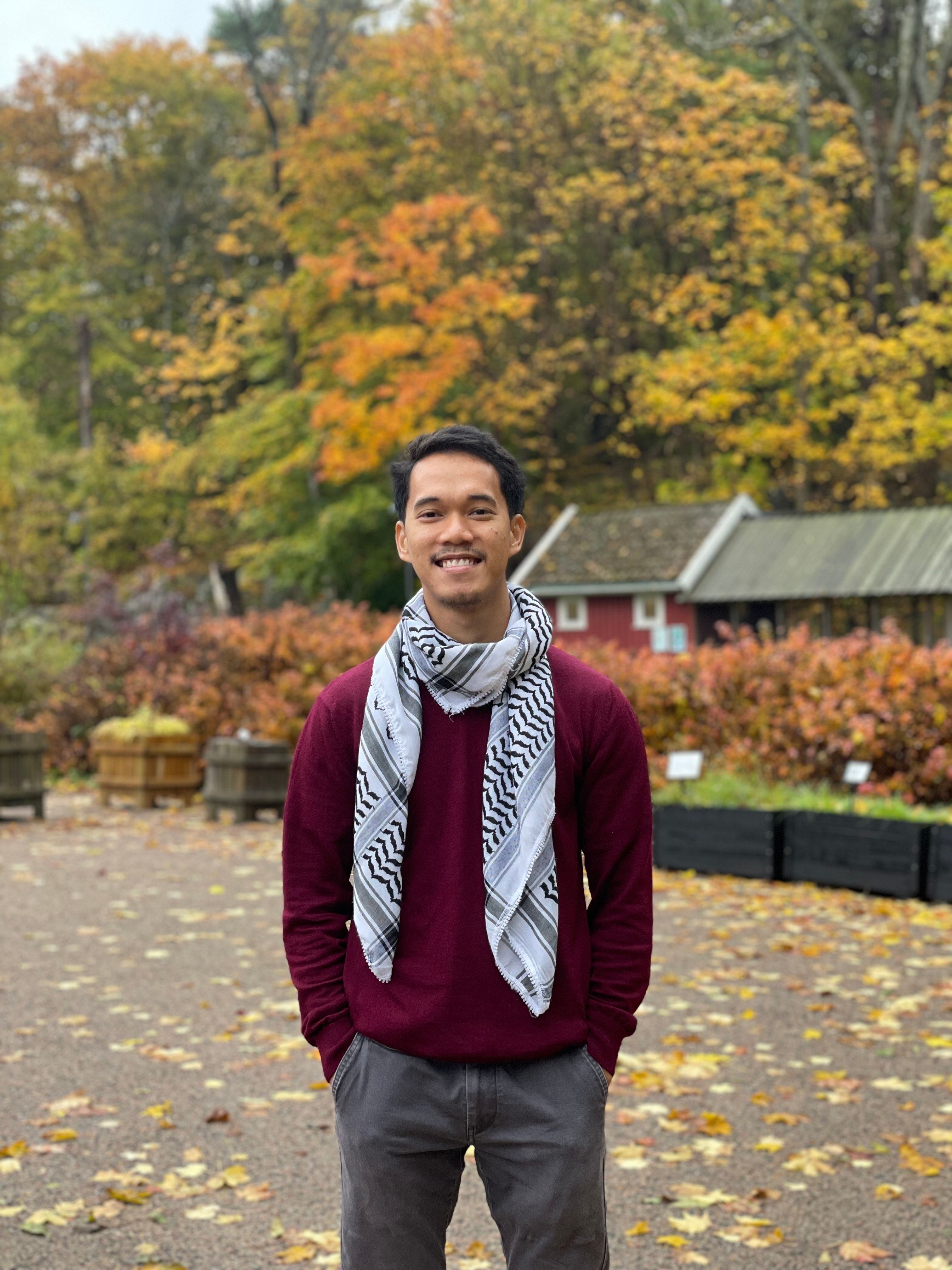 a man wearing a scarf and a maroon sweater poses for a picture