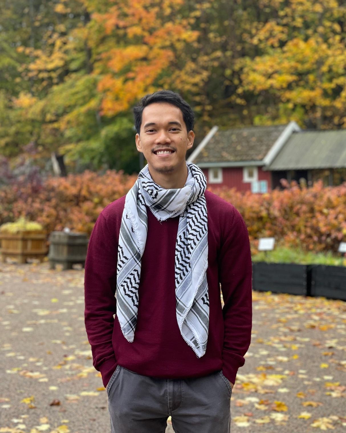a man wearing a scarf and a maroon sweater poses for a picture