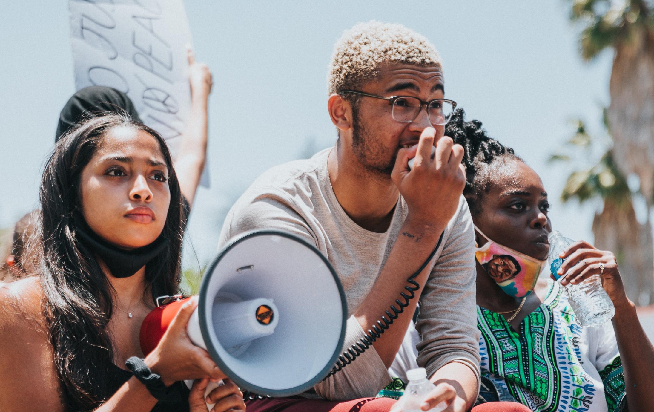 Three students holding a megaphone. Illustration from Unsplash. 