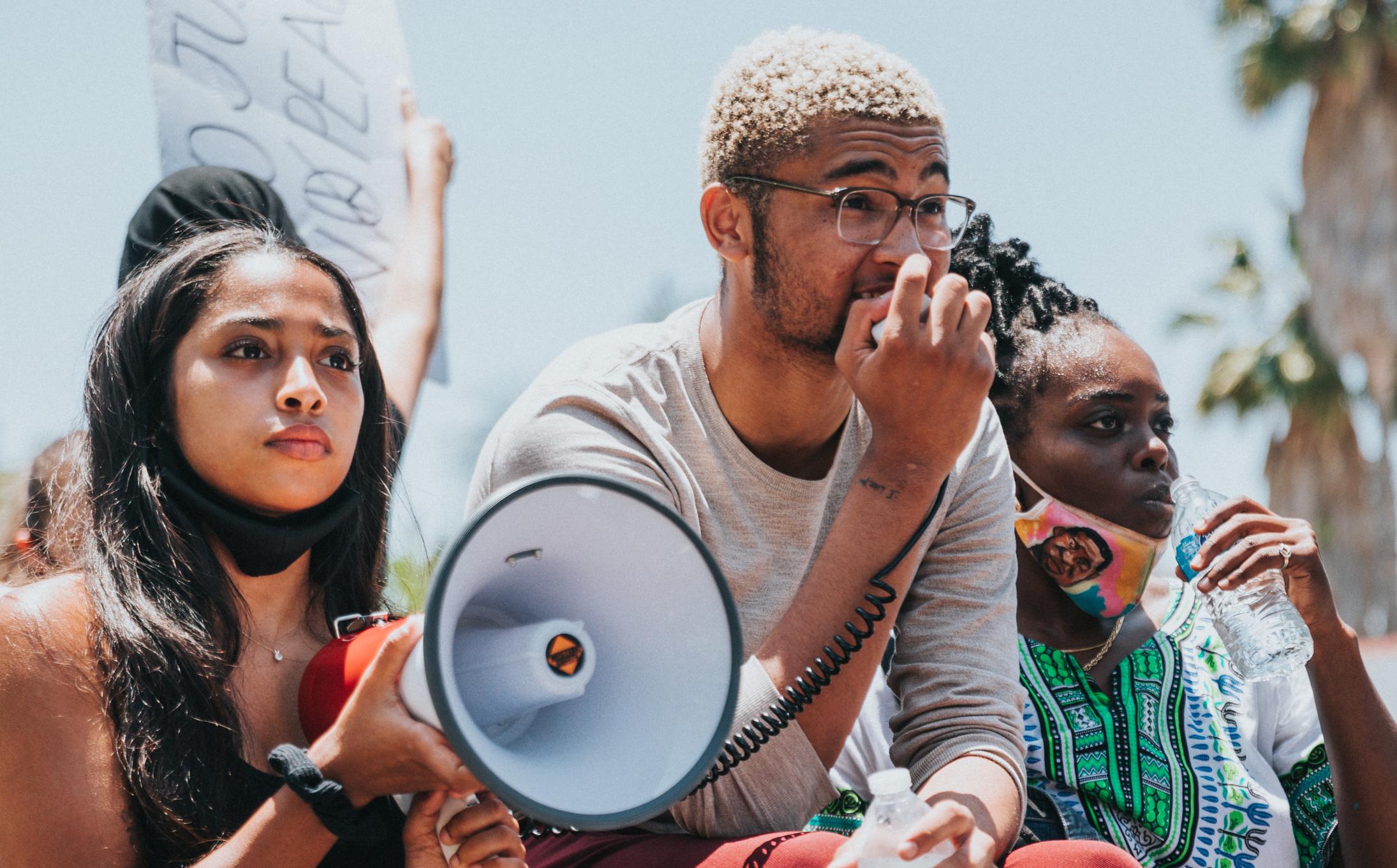 Three students holding a megaphone. Illustration from Unsplash. 