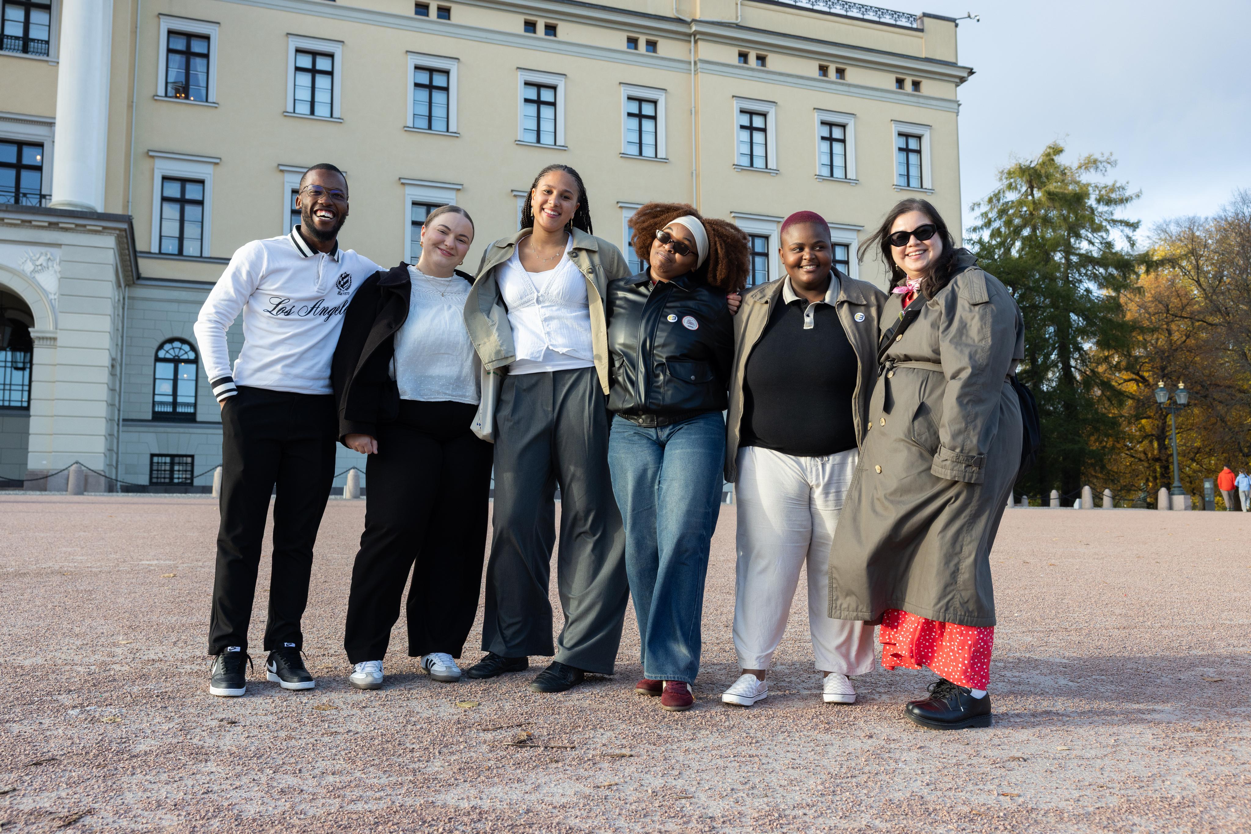 A diverse group of six people smiling in front of a grand building.