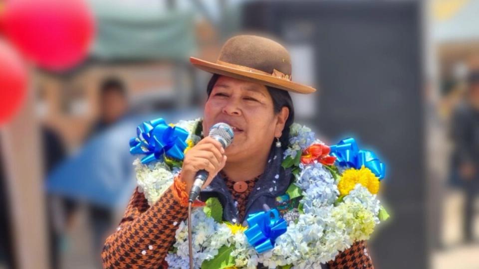 En kvinne med hatt og blomsterkrans holder en mikrofon i hånden.