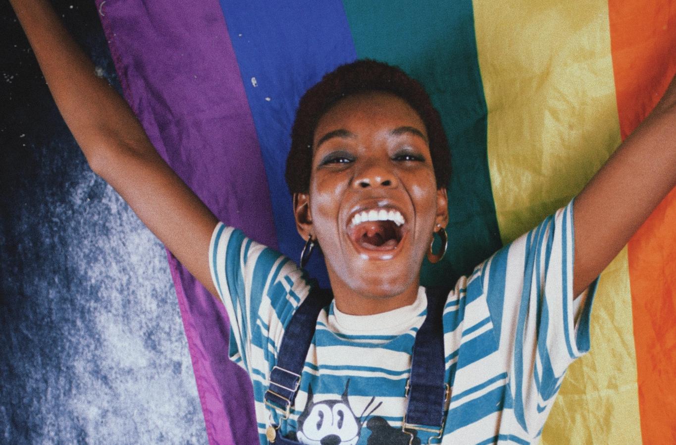 A woman holds up a rainbow flag and cheers. Illustration image from Unsplash.
