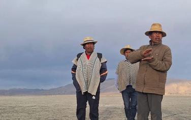 Three men stand on a dry crust of land where the lake once was.
