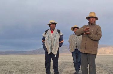 Three men stand on a dry crust of land where the lake once was.