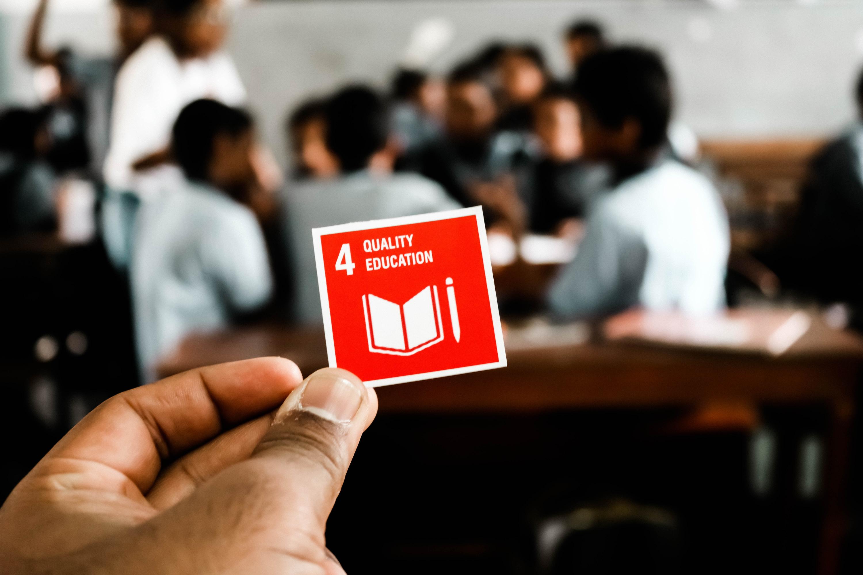 A person holding up a sticker with the logo for the UN`s sustainable development goal 4 - quality education