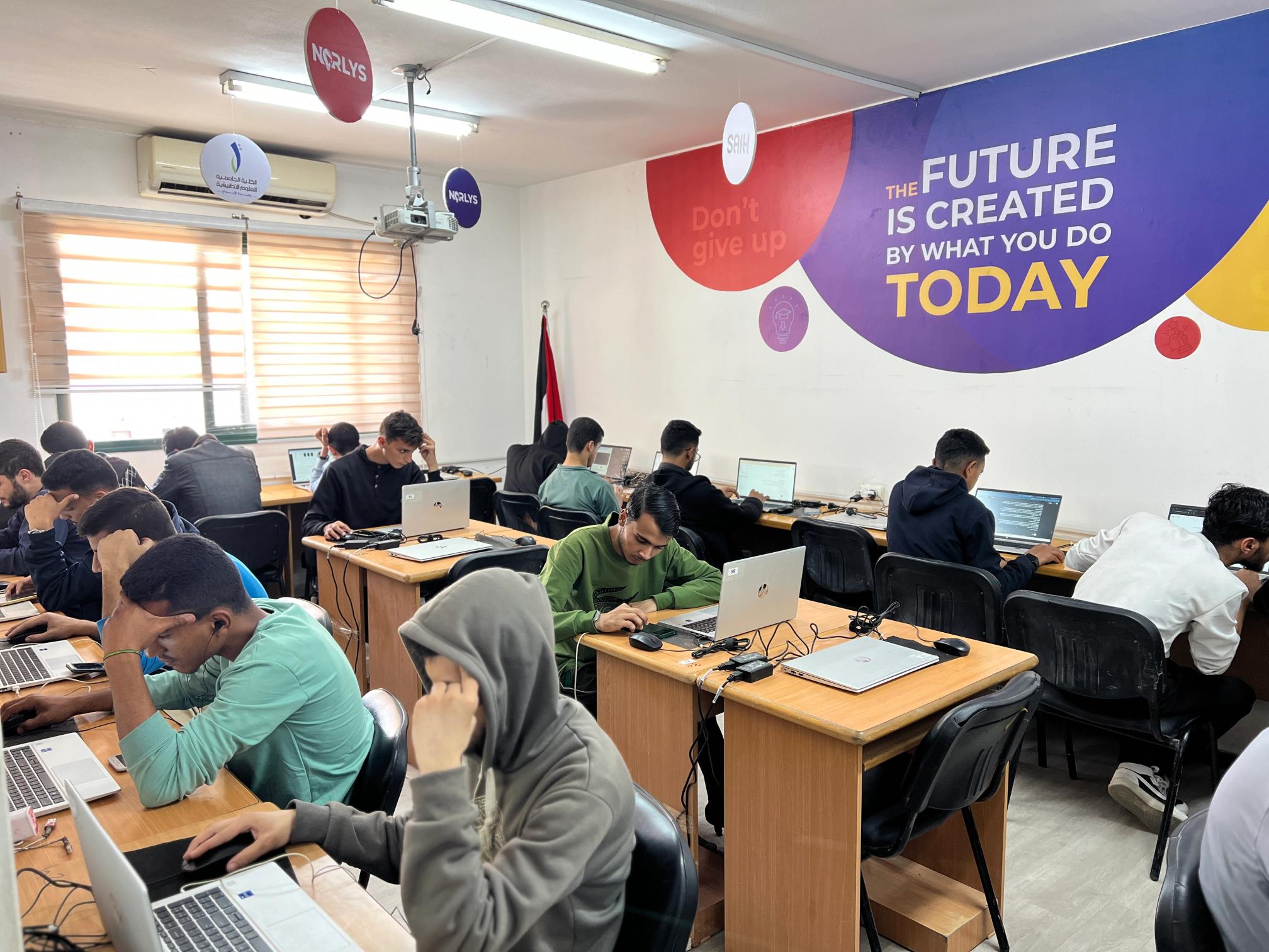 A classroom of students working on laptops, with a motivational mural on the wall.