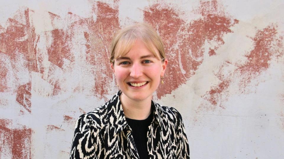 a woman wearing a yellow vest and earrings is smiling for the camera .