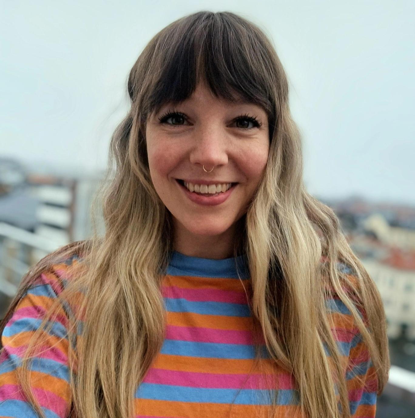 a woman wearing a striped shirt and a nose ring is smiling for the camera .