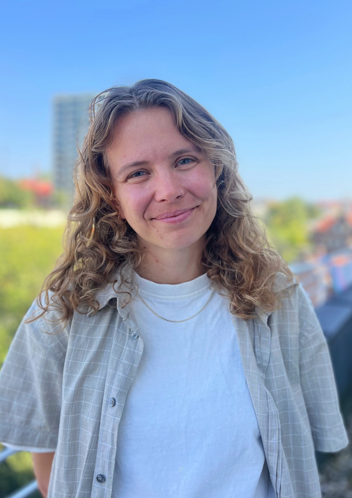 a woman with curly hair and a plaid shirt smiles for the camera