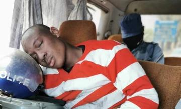 Takudzwa Ngadziore sits in a police car and rests his head on a police helmet.