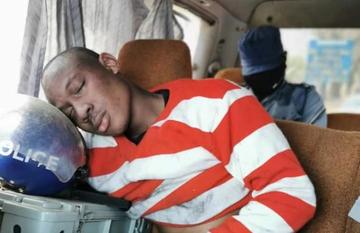 Takudzwa Ngadziore sits in a police car and rests his head on a police helmet.