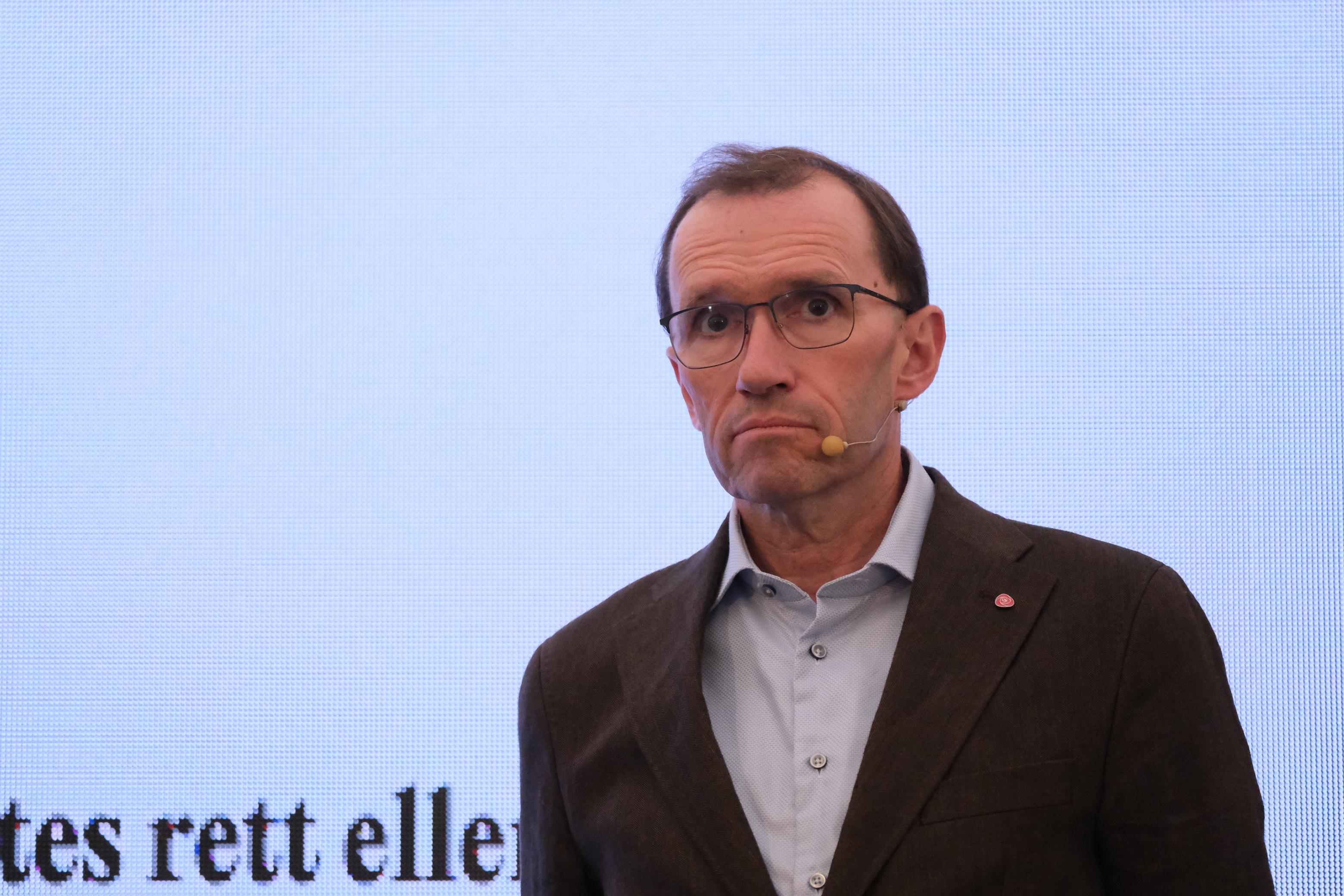 a man wearing glasses and a suit is standing in front of a microphone .