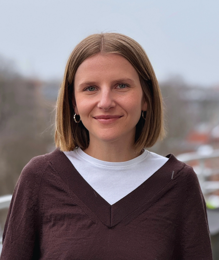 a woman wearing a brown sweater and a white shirt smiles for the camera