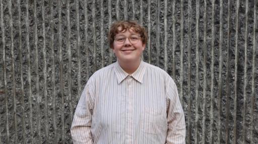 a young women wearing glasses and a striped shirt is standing in front of a stone wall .