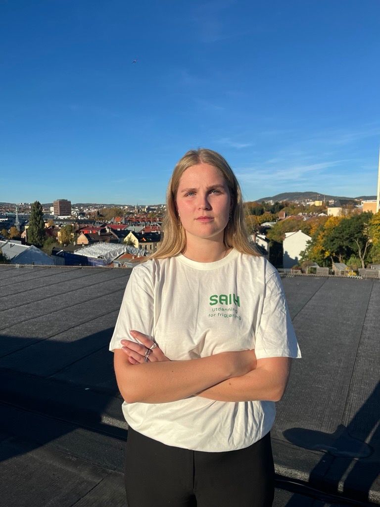 ung kvinne står med armene i kryss og ser alvorlig inn i kamera