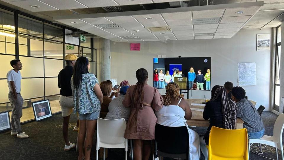 A group of people watching a panel discussion on a large screen.