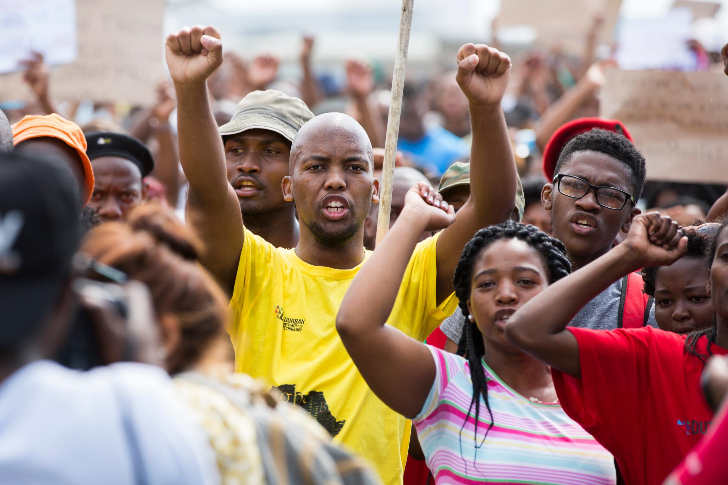 Young people participate in a protest with fists raised in the air.