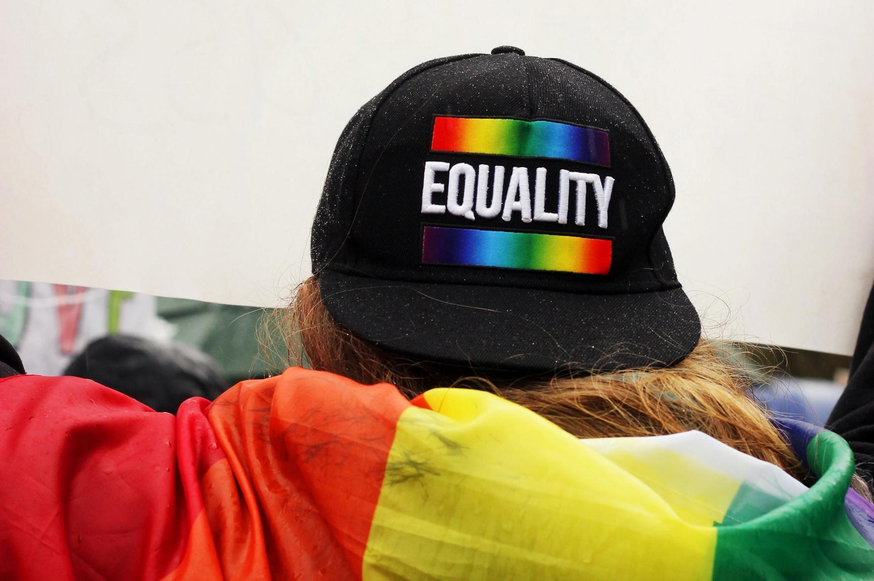 En person med LHBT-flagg over ryggen og en caps med teksten "likhet". 