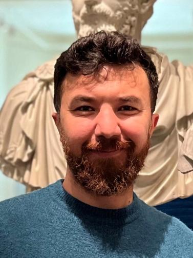 a man with a beard is smiling in front of a statue