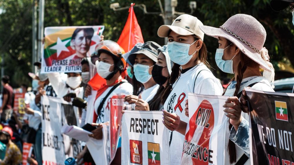 Mennesker iført munnbind, holder opp flagg og plakater med bilde av det burmesiske flagget og Aung San Suu Kyi.