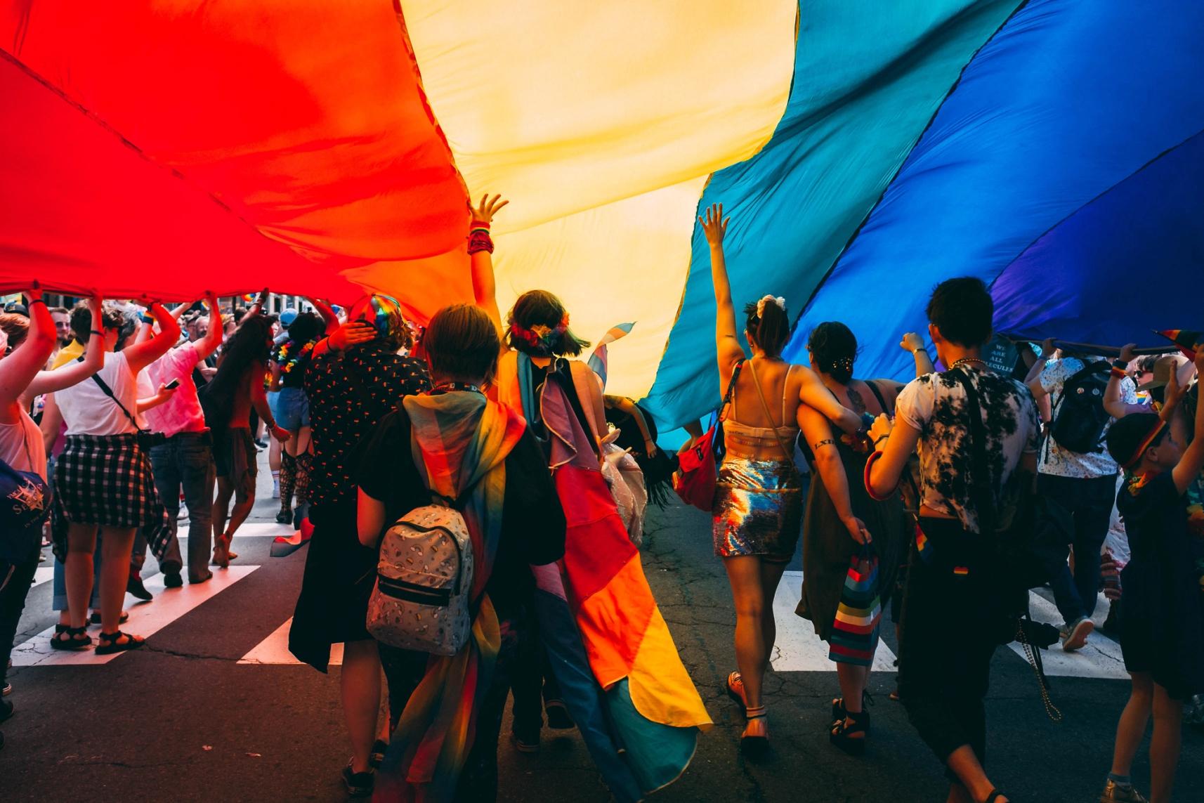 A group of people holding a large rainbow flag over them.
