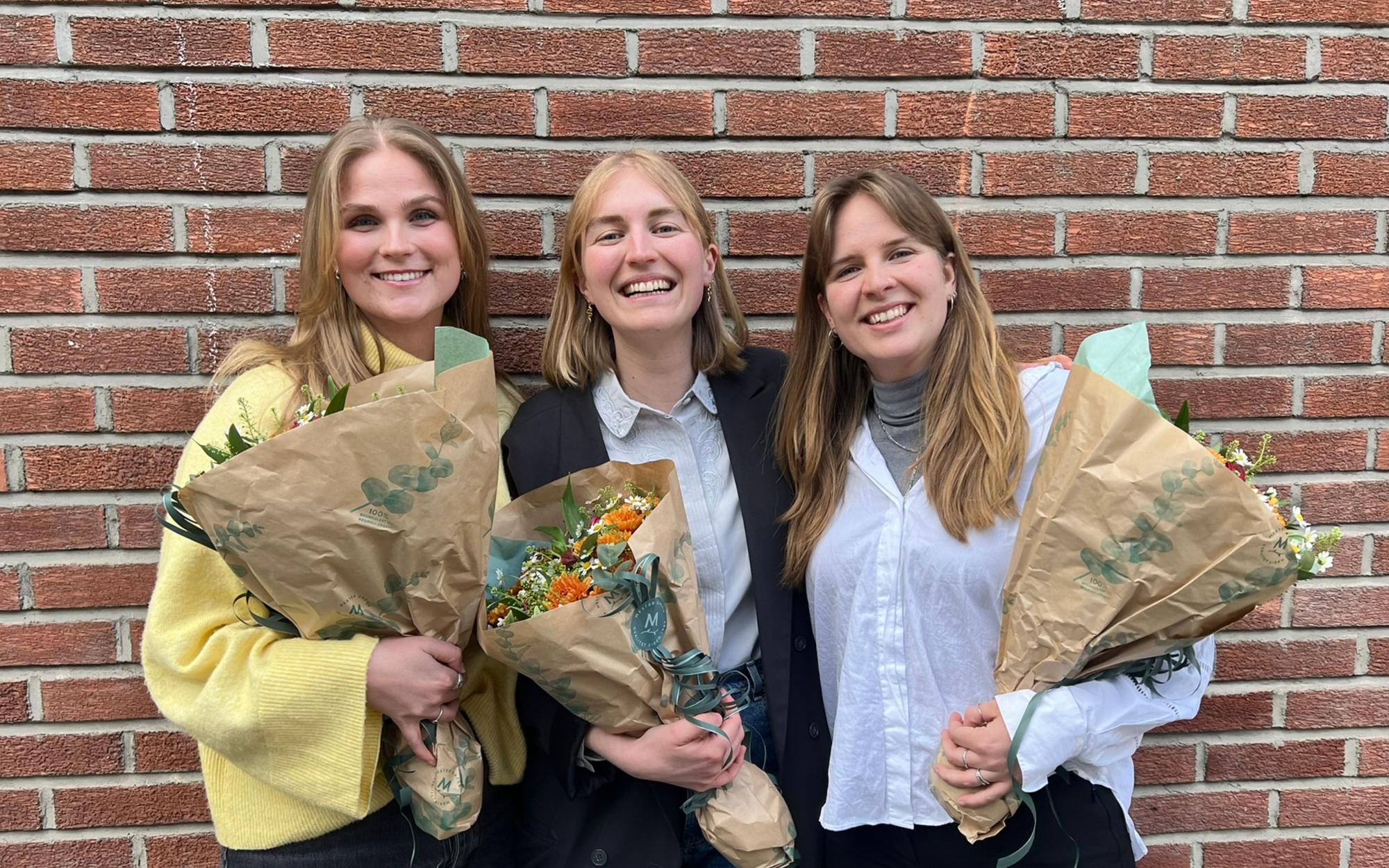 Tre kvinner står ved siden av hverandre med blomster i hendene.