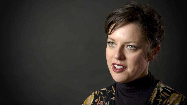 A woman in front of a black background, speaking into the camera.