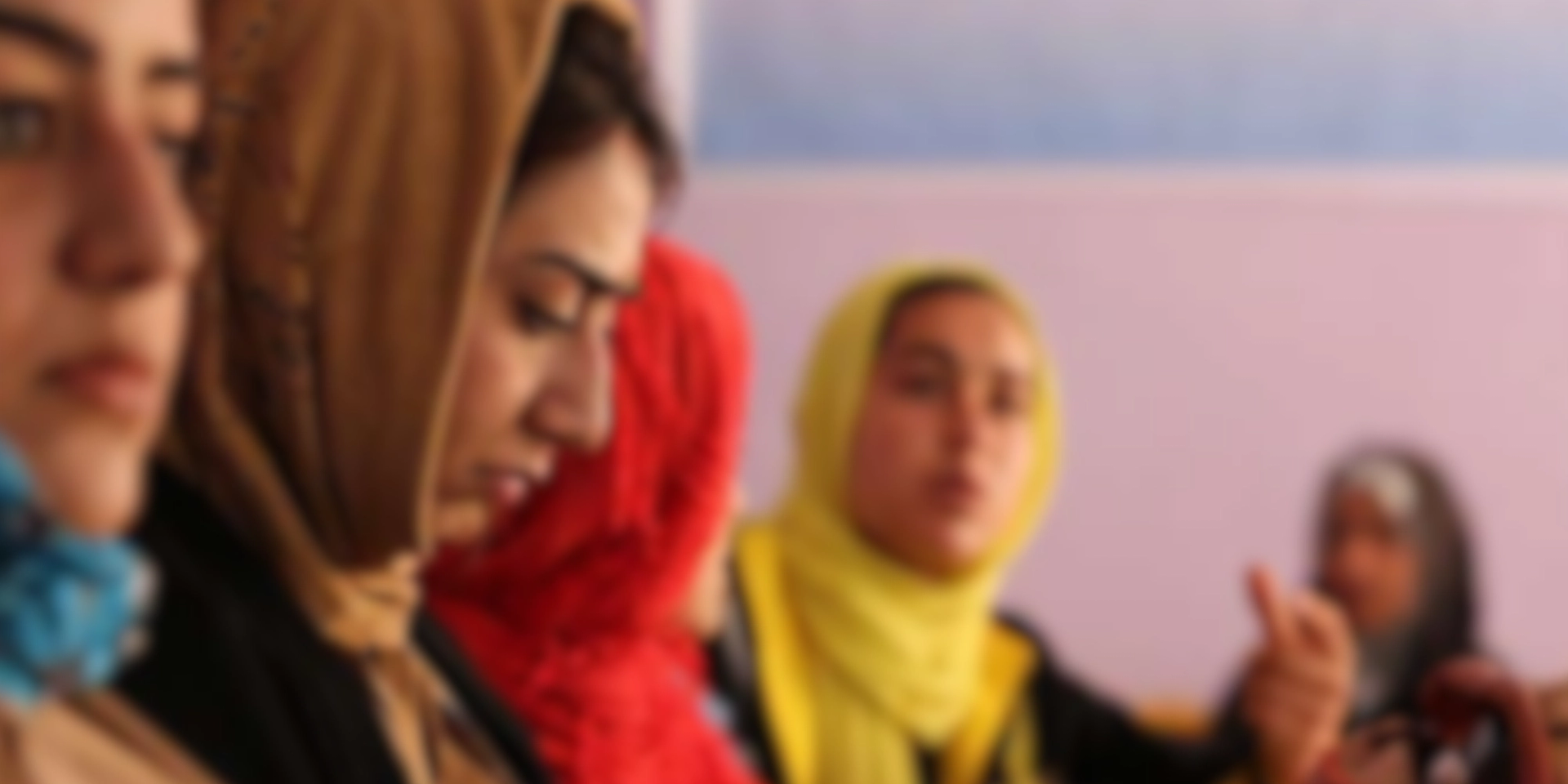 Several women wearing headscarves, with one in the foreground looking left.