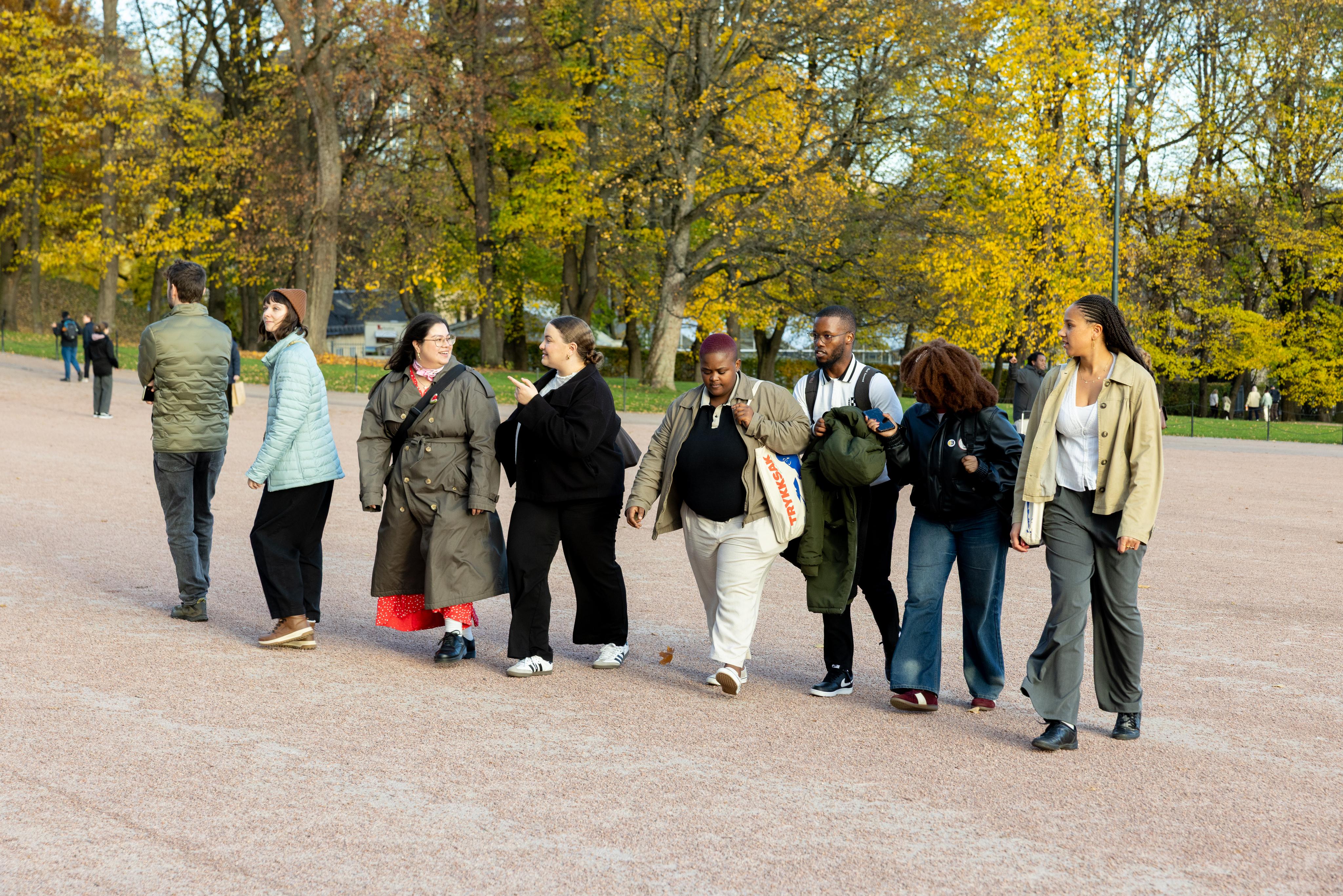 A diverse group of people walking on a path in a park with golden autumn trees.