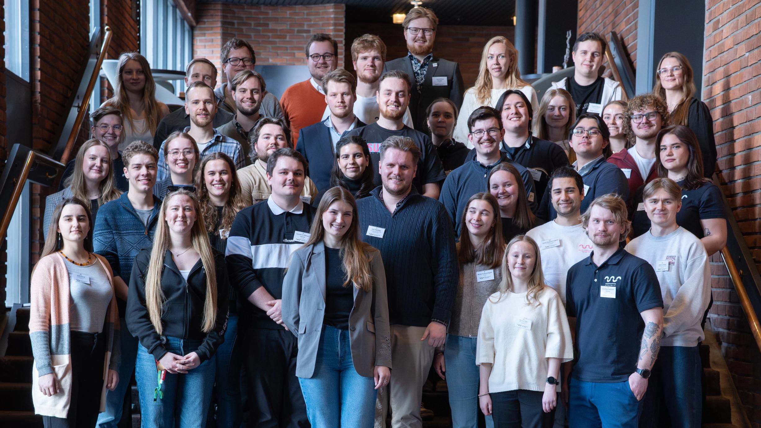 A large group of smiling young adults pose on a staircase, many wearing name tags.