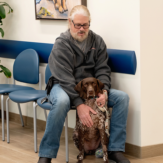 A man sitting on a blue chair with a German shorthair pointer dog.