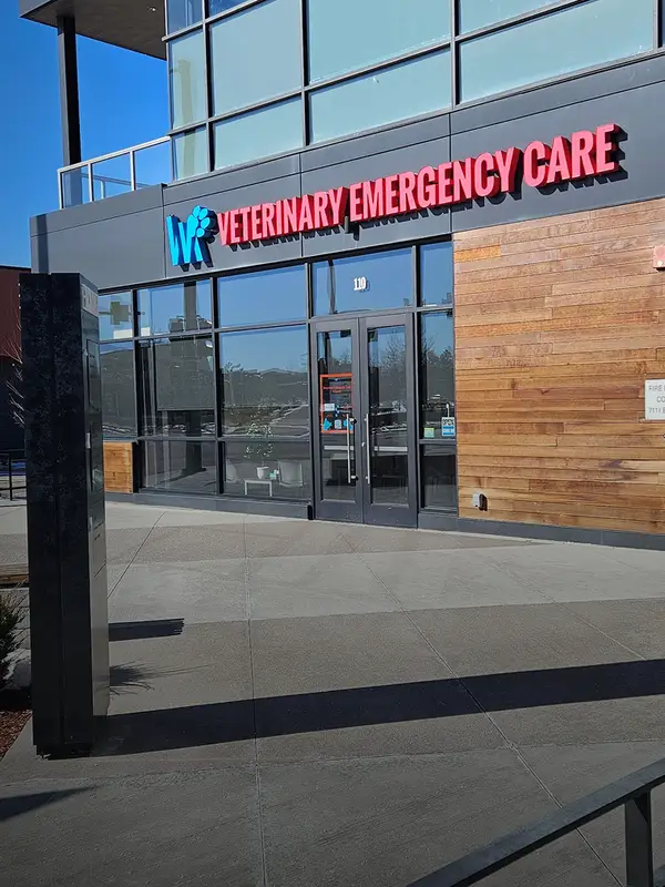 Entrance of a veterinary emergency care facility with glass doors and red signage.