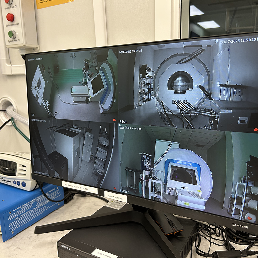 A Hallmarq MRI machine viewed through a window, with a monitor showing multiple angles of the machine.