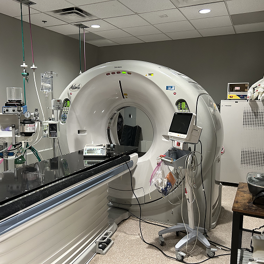 A CT scanner in a medical room with medical equipment and a patient table.