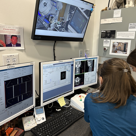A clinical setting with four monitors displaying technical images and two veterinary staff analyzing them.