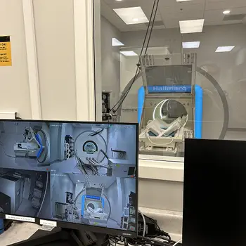 A Hallmarq MRI machine viewed through a window, with a monitor showing multiple angles of the machine.