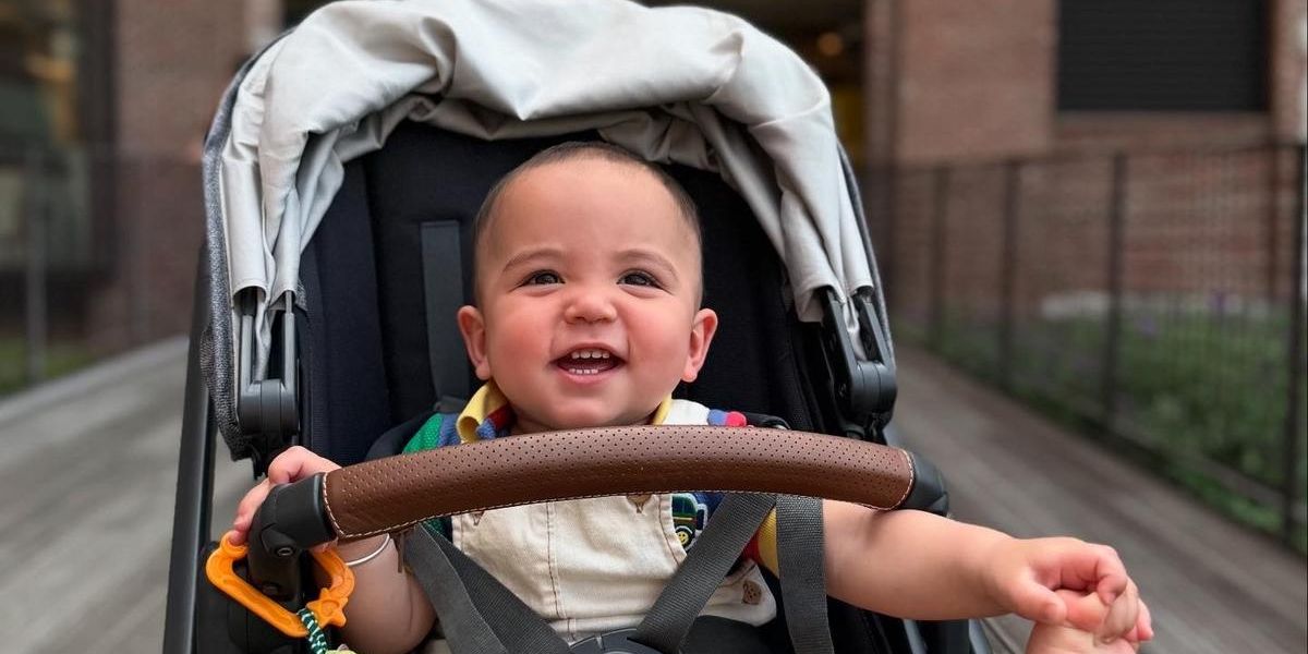 Jaxon smiling in a stroller at the Atlanta BeltLine in front of Ponce City Market