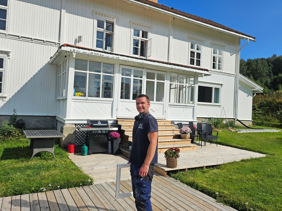 Pål Erik Hansveen står foran et trehus i solskinn.