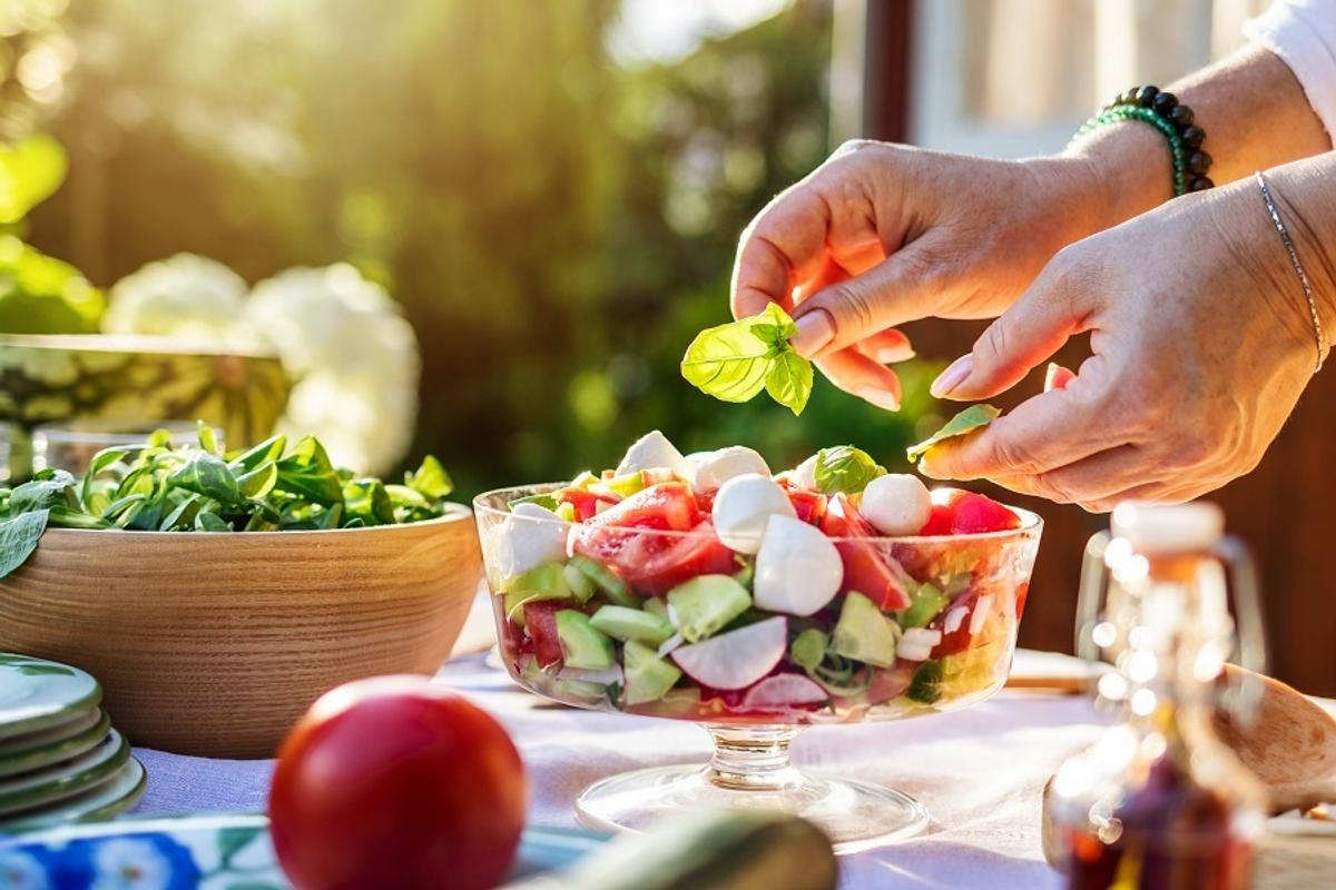 Eldre kvinne legger basilikum på en fargerik salat.