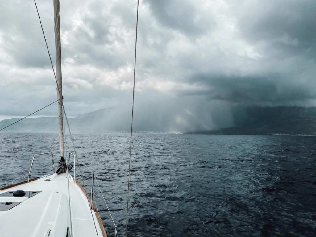 A sailboat drifting towards a storm in the distance.