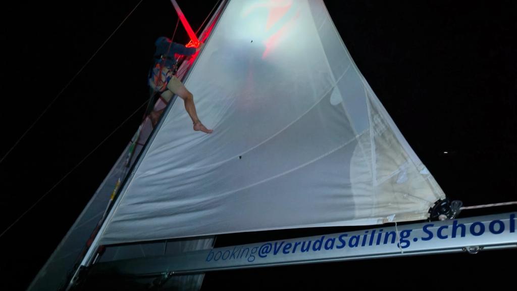 A crew member up Buri's mast at night, securing the rig