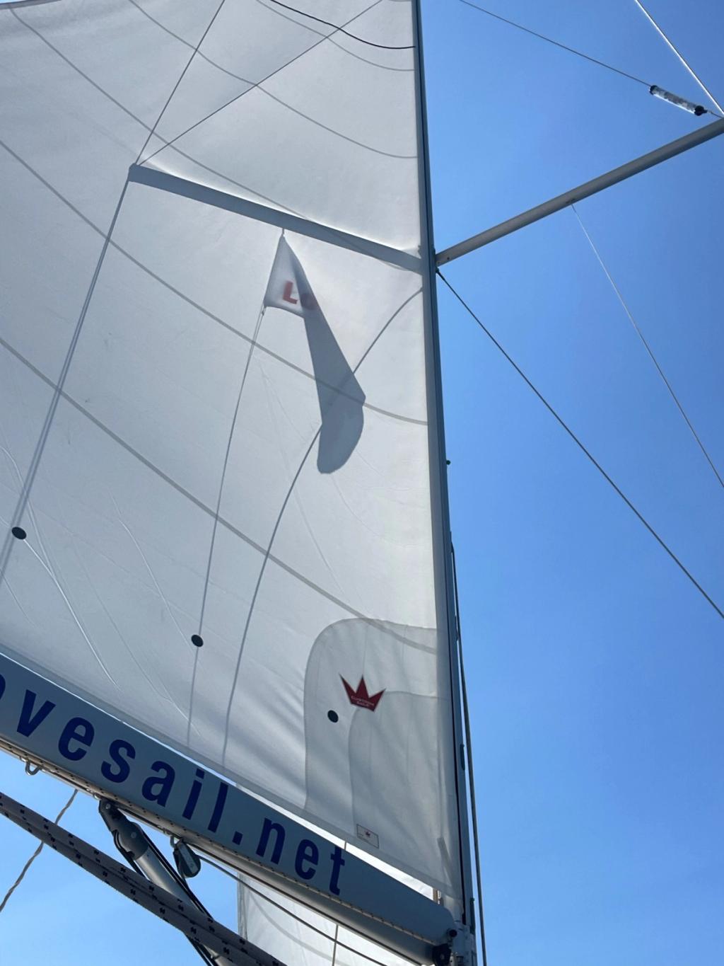 Close-up of a white mainsail illuminated by sunlight against a clear blue sky.