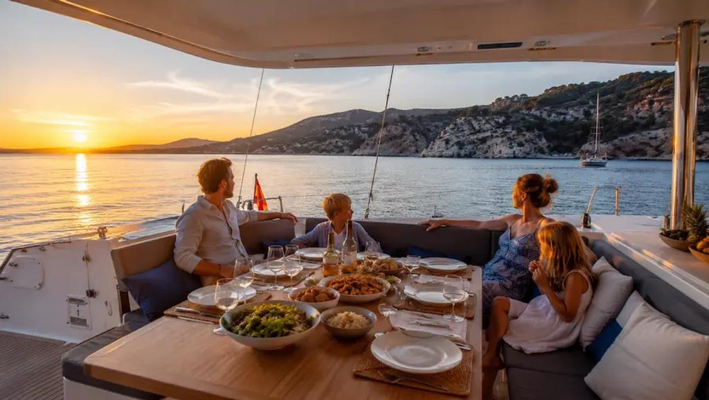 Family relaxing at a level dinner table on a catamaran's wide cockpit at anchor
