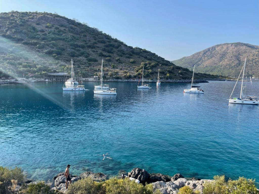 Sailboats anchored in a calm turquoise bay surrounded by green hills