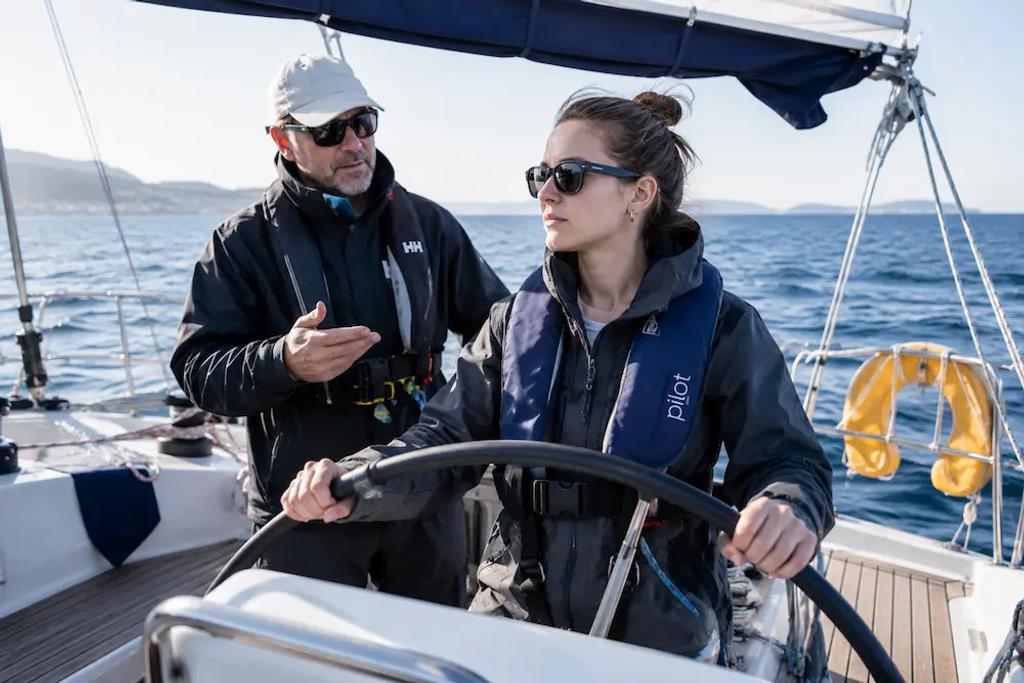 Beginner sailor steering a sailboat for the first time with an instructor nearby