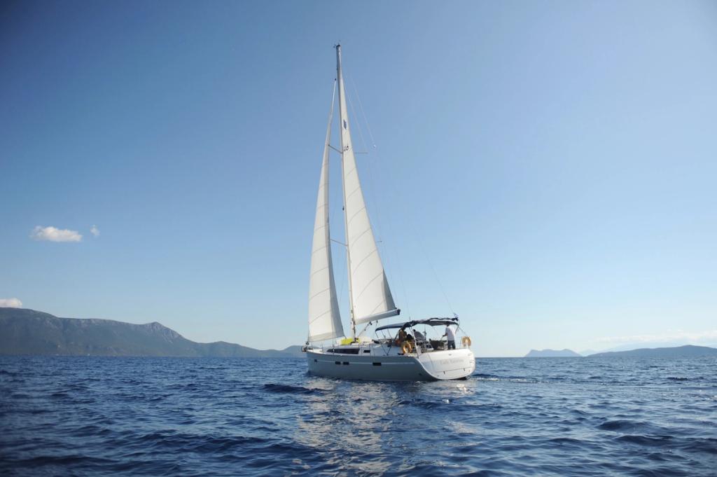 A sailboat on very calm water, sun shining and no clouds in the sky.