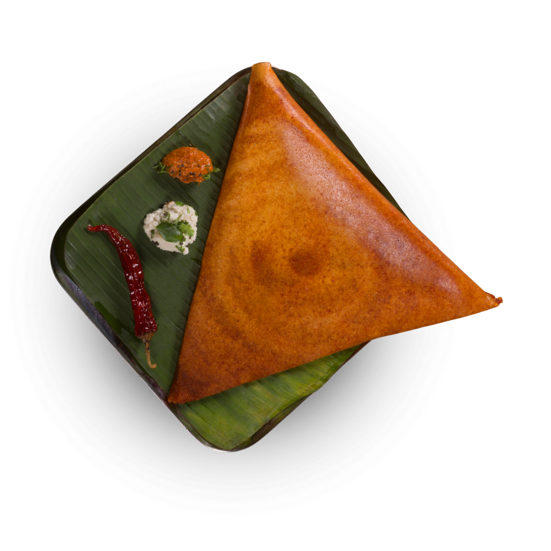 Crispy golden masala dosa served on a banana leaf with coconut chutney, tomato chutney, and a whole dried red chili.