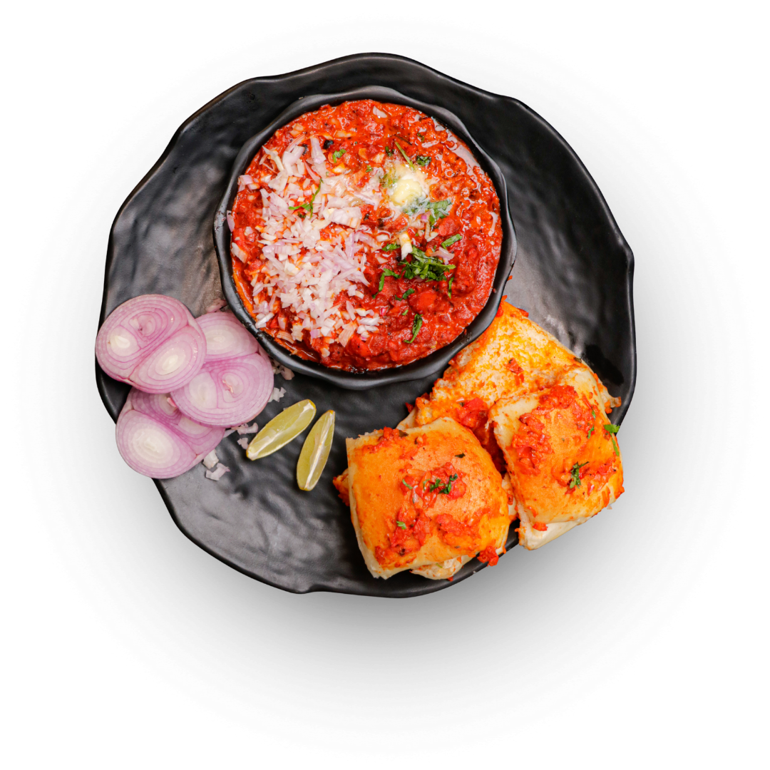 Spicy Mumbai-style pav bhaji served with buttered pav, chopped onions, lemon wedges, and a dollop of butter on top.