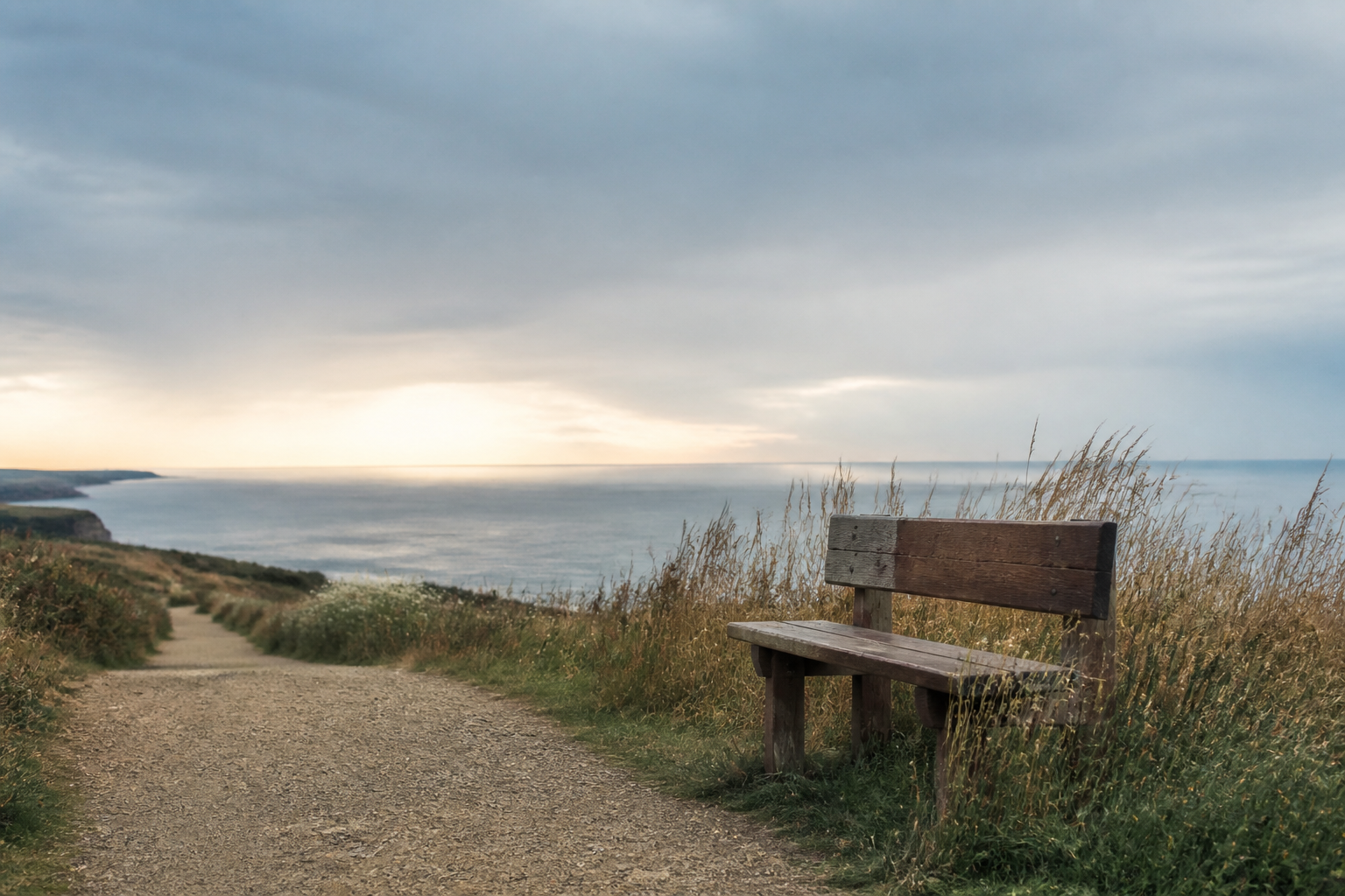 A quiet coastal path leading past a wooden bench toward an open horizon